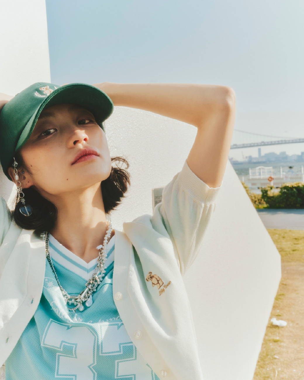 Lily Bearキャップ・Lily Bearハーフスリーブカーディガン・Lily Bearリブソックス・サイドレースナンバリングTシャツ・カーブドロストハーフデニムパンツ・サテンハートパンプス・ビジューミニショルダーバッグ・バリエーションスリーピン・メタルコンビパールネックレス・2WAYチェーンチャームネックレス・モチーフチェーンバッグチャームを着用した女性