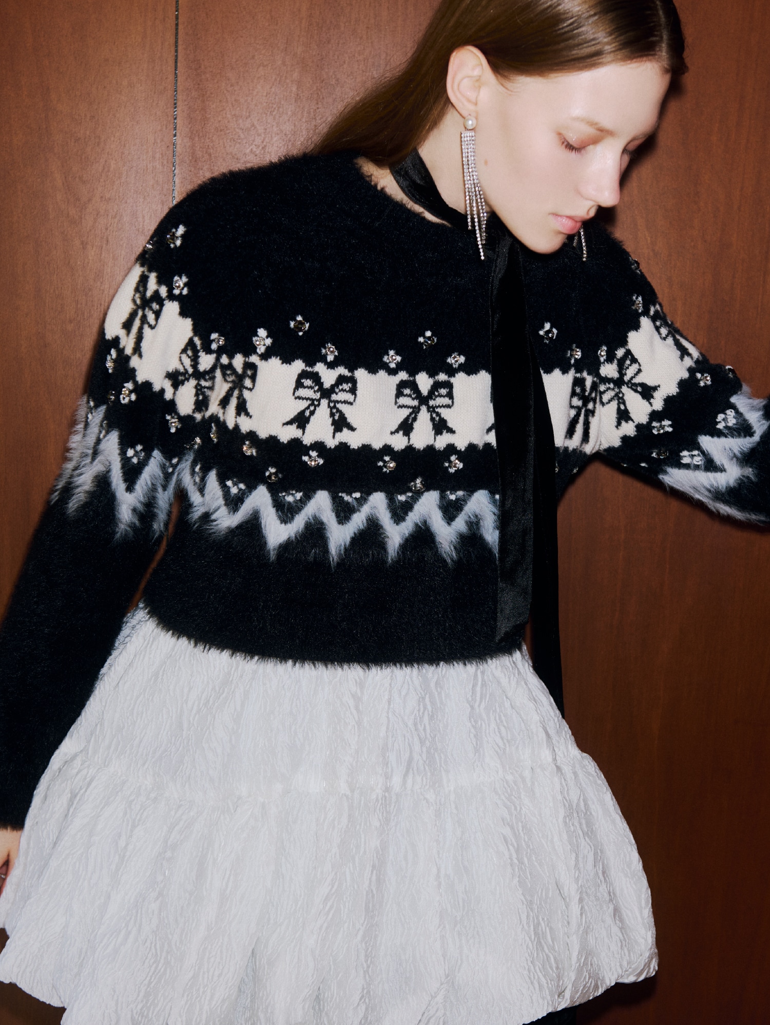 リボンの編み地とビジューがついた黒と白のニットトップスと白のシーア素材のミニワンピースを着た女性