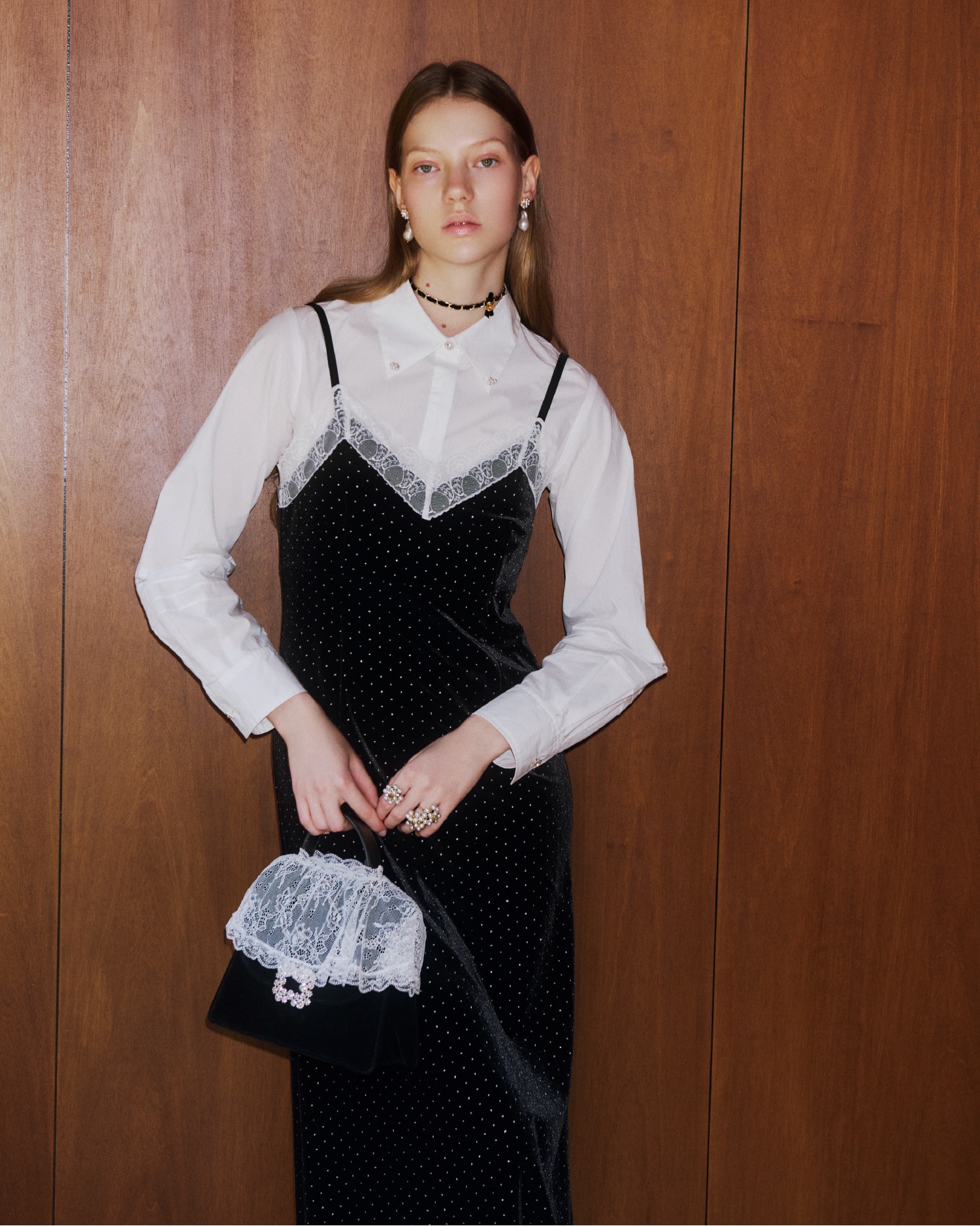 黒のシャツコンビビジューワンピースを着て白いレースがかぶさった黒いバッグを持つ女性。パールのピアスと黒のベルベッドリボンの二連ネックレスの着用例