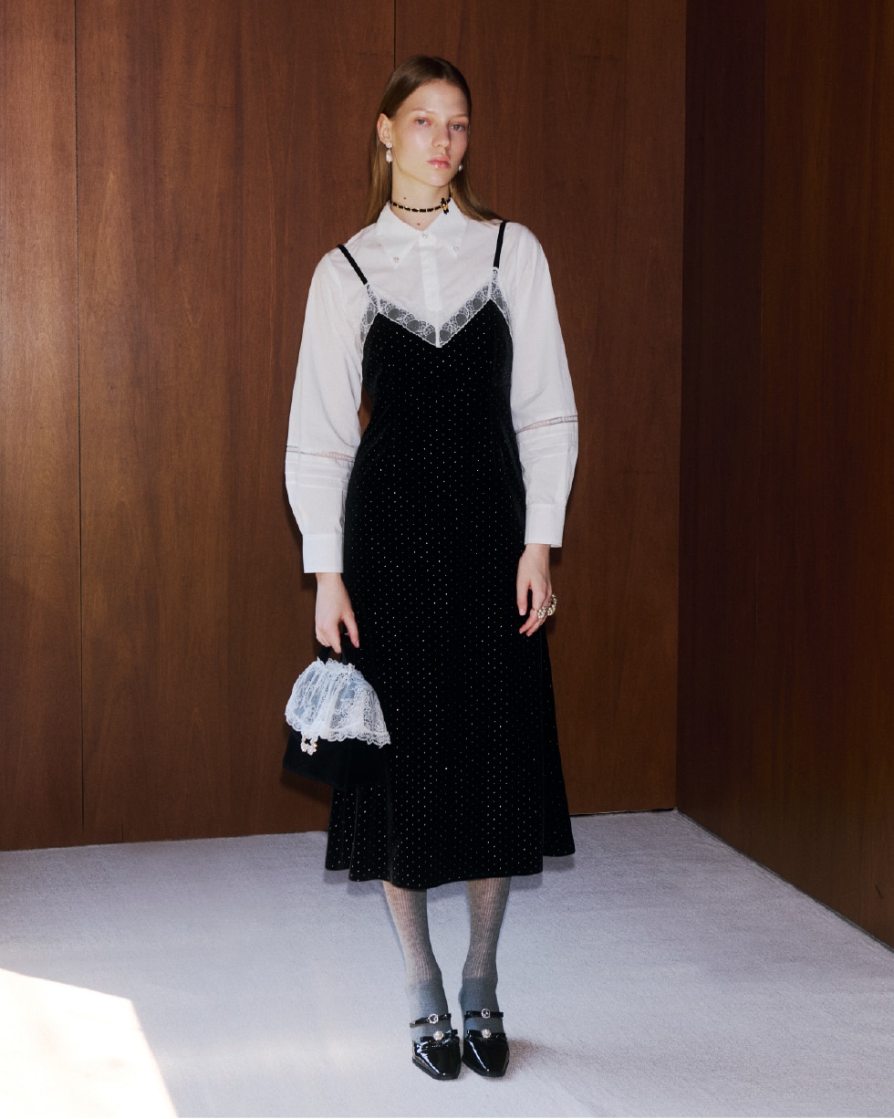 黒のシャツコンビビジューワンピースを着て白いレースがかぶさった黒いバッグを持つ女性。パールのピアスと黒のベルベッドリボンの二連ネックレスの着用例