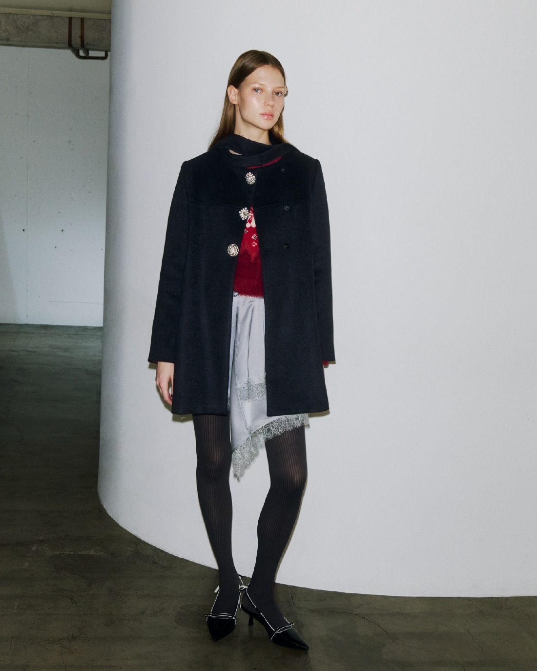 ボタン部分にビジューがあしらわれたダークネイビーのコートとビジューのニットトップ、グレーのサテン地のミニスカートの着用例