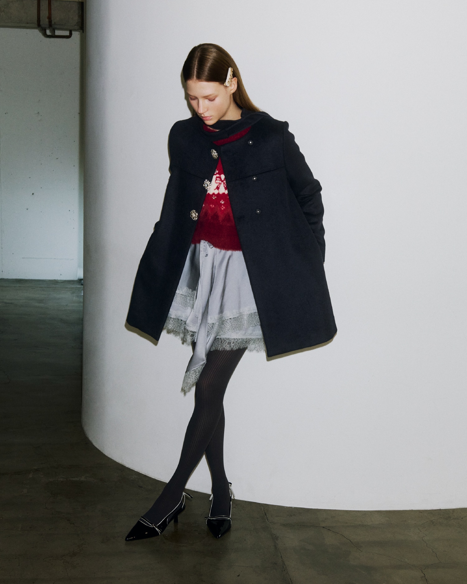 ボタン部分にビジューがあしらわれたダークネイビーのコートとビジューのニットトップ、グレーのサテン地のミニスカートの着用例