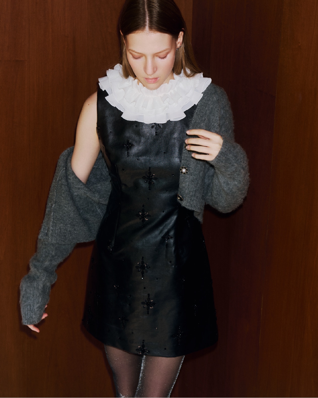 黒のミニワンピースとビジューが施されたグレーのビジューニット、黒のレースアップバレエシューズの着用例