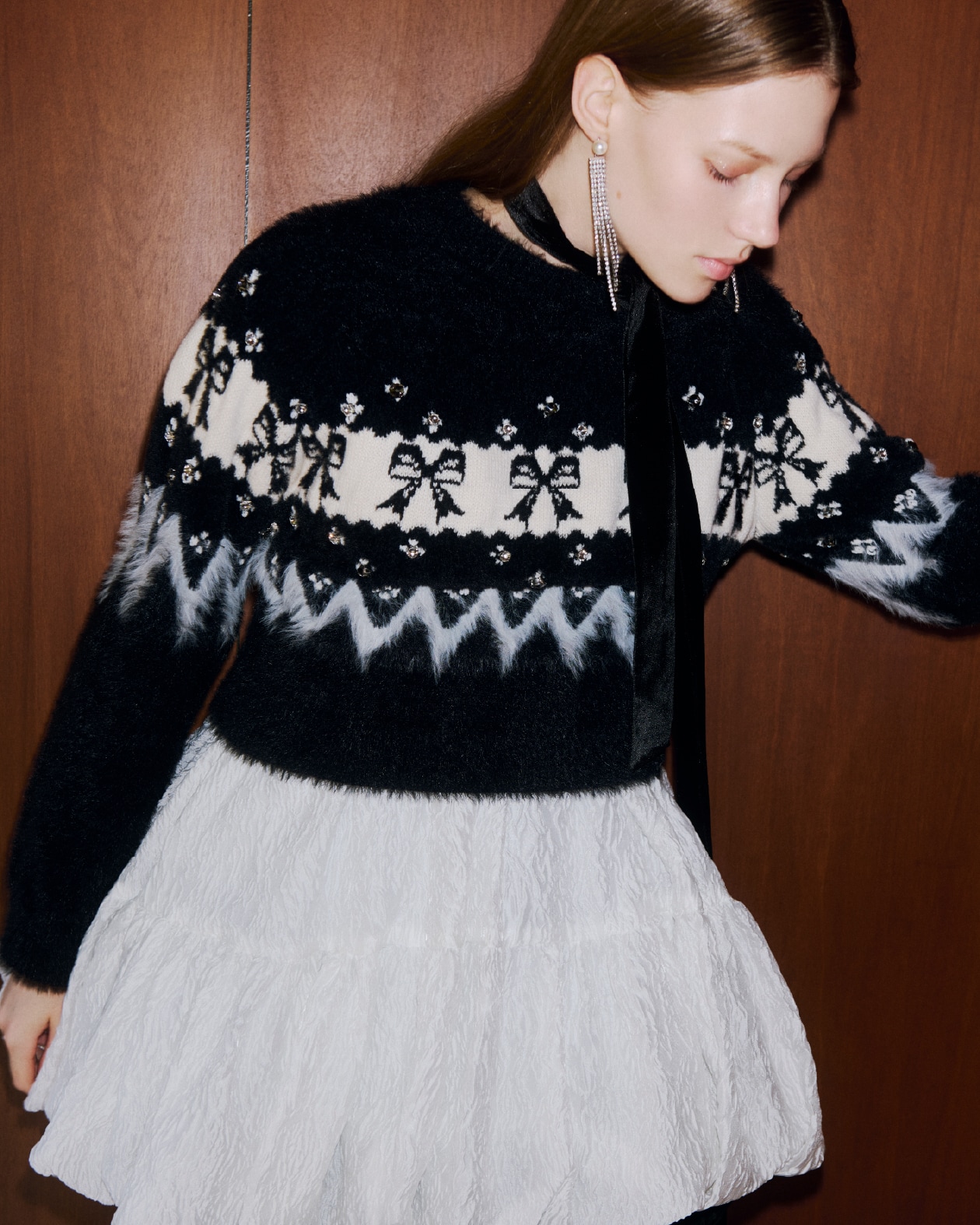 リボンの編み地とビジューがついた黒と白のニットトップスと白のシーア素材のミニワンピースを着た女性