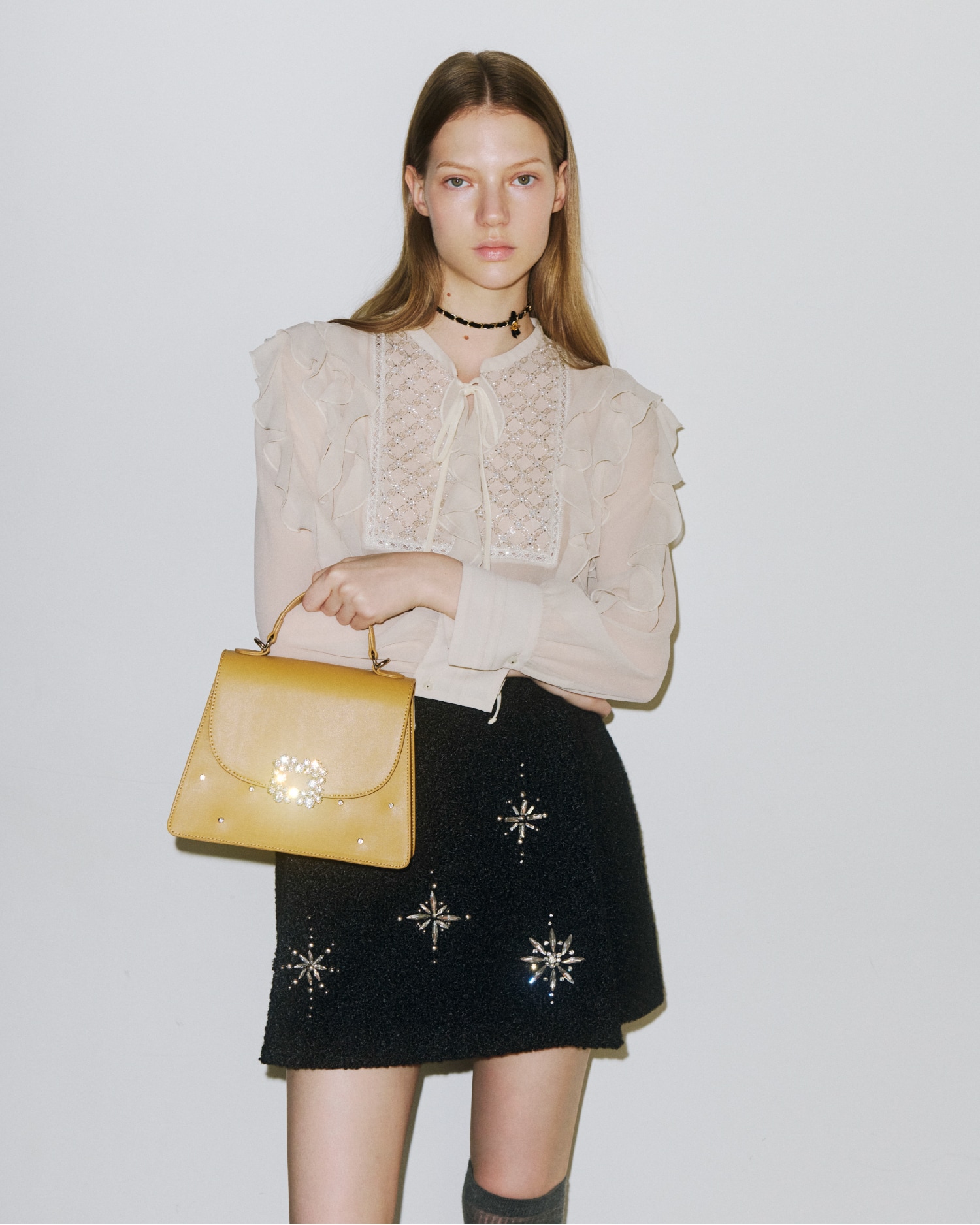 ブザムにビジューがあしらわれたベージュのフリルブラウスと、雪の結晶のビジューがあしらわれた黒のミニスカートの着用例