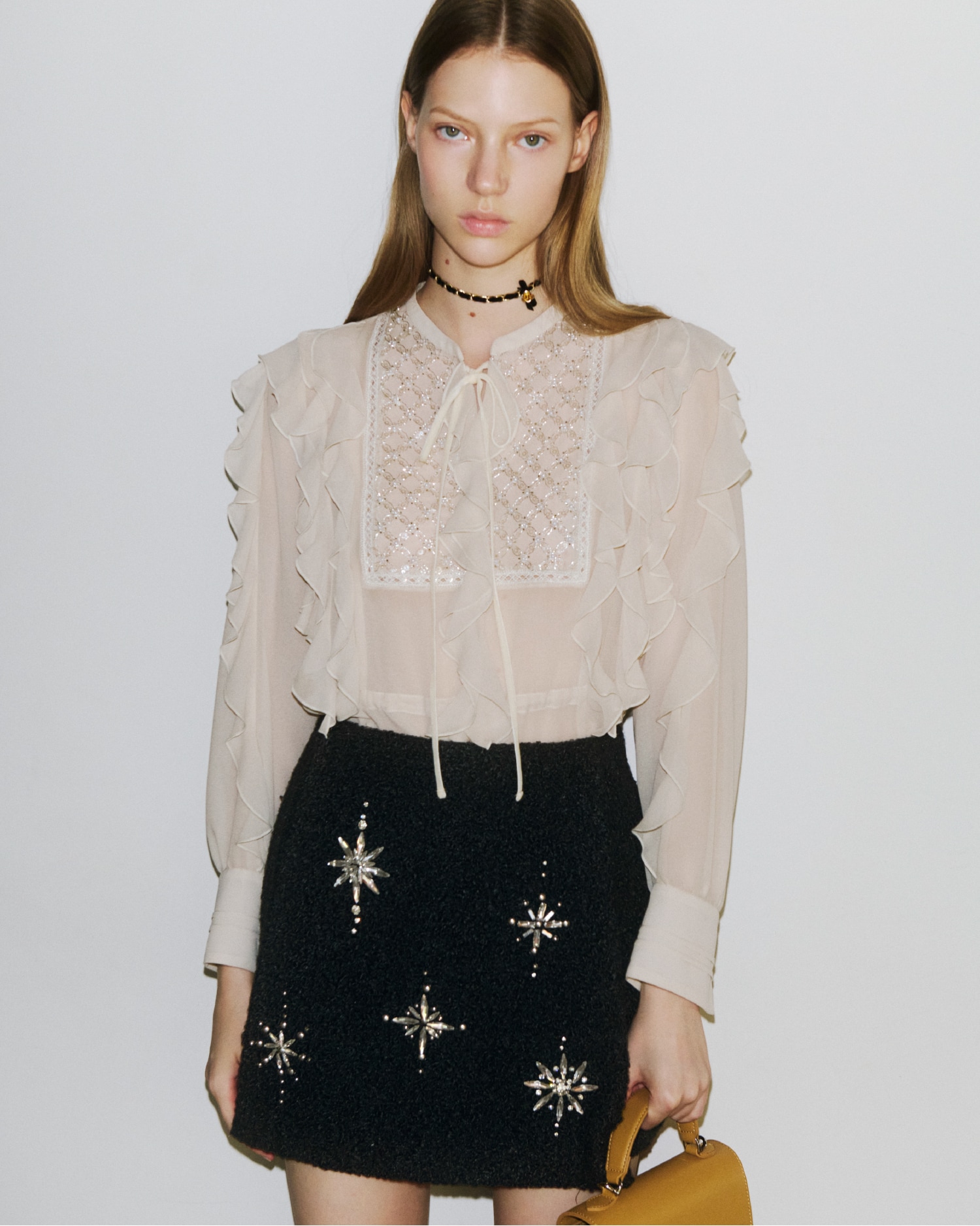 ブザムにビジューがあしらわれたベージュのフリルブラウスと、雪の結晶のビジューがあしらわれた黒のミニスカートの着用例