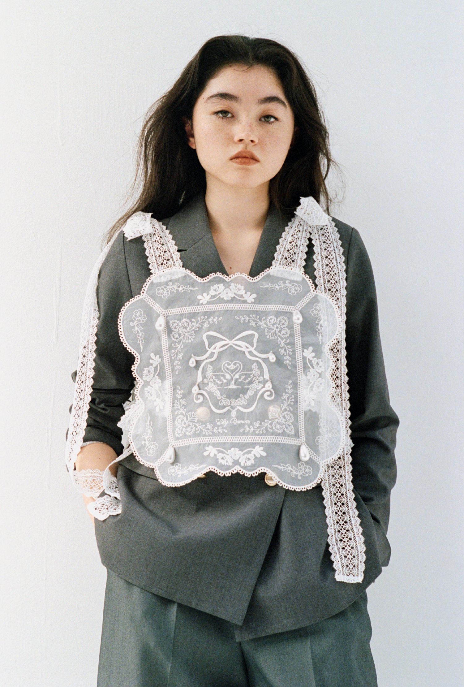 白の[L.B CANDY STOCK]ビジューエプロン・グレーのダブルブレストジャケットとベルト付きバックスリットパンツを合わせた、洗練されたラグジュアリーなコーディネート