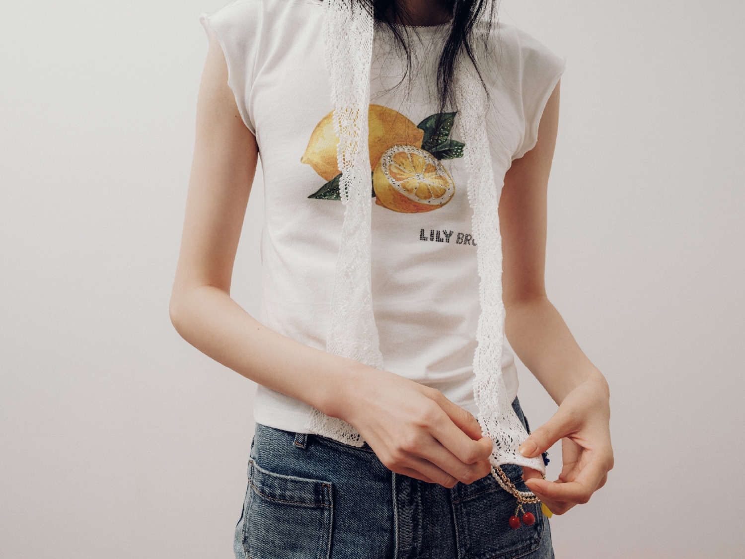 イエローのフルーツビジューTシャツ・ライトブルーのストレッチセミフレアデニムパンツ・アイボリーのビーニー・白のスカーフ・チャーム・黒のパンプスを合わせたコーディネート