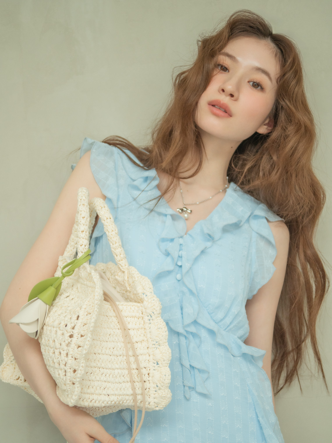 水色のフリルドレスを着て白いバッグを持つモデルの上半身