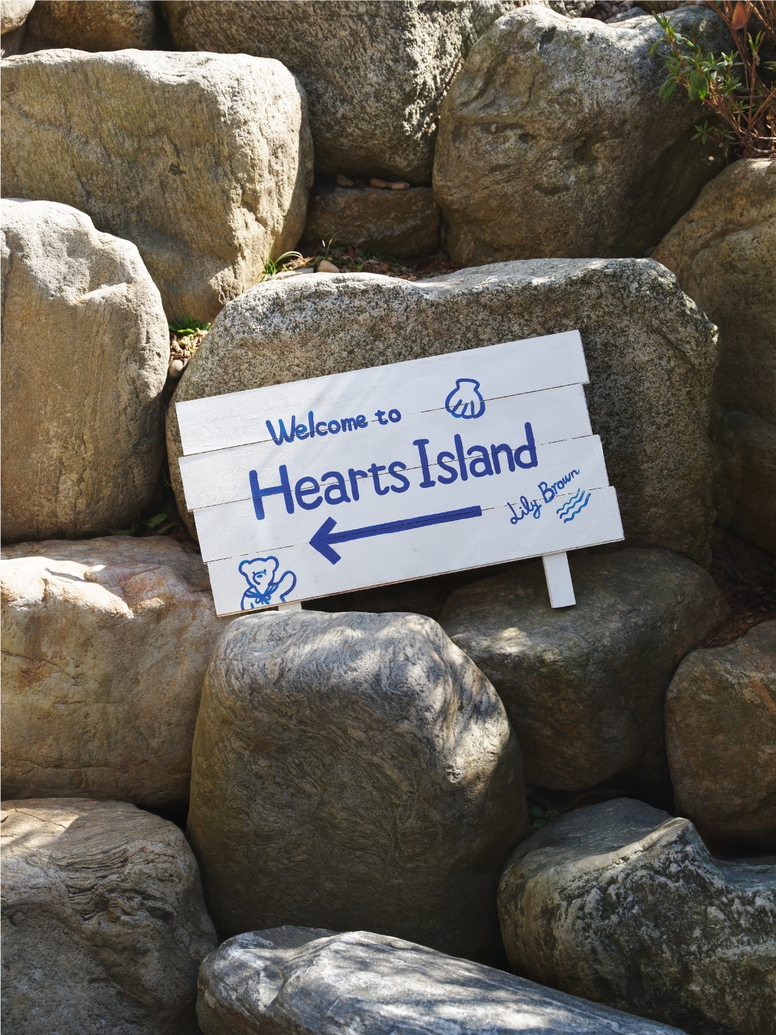 岩場に置かれたWelcome to Hearts Islandの白い看板のイメージビジュアル