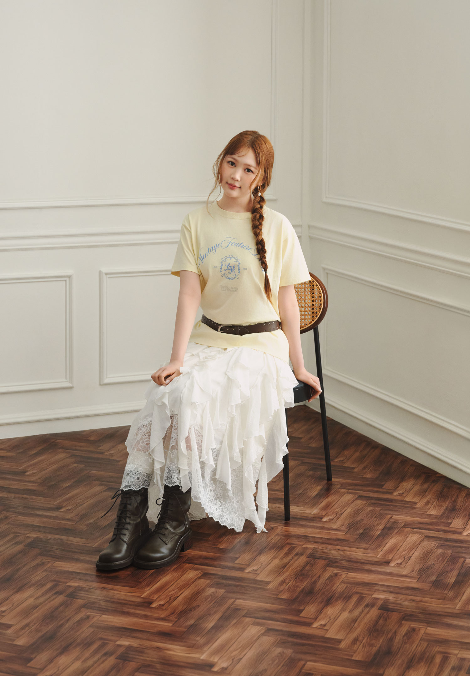 黄色のロゴTシャツと白いチュールスカートを着用し、椅子に座る女性モデルの全身カット
