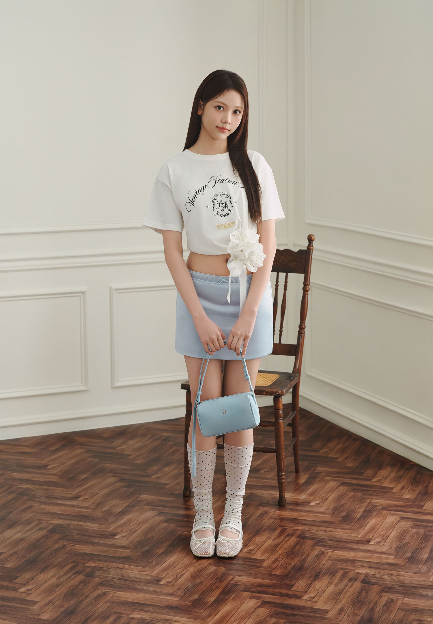 白いロゴTシャツと水色のミニスカートを着用した女性モデルの全身カット