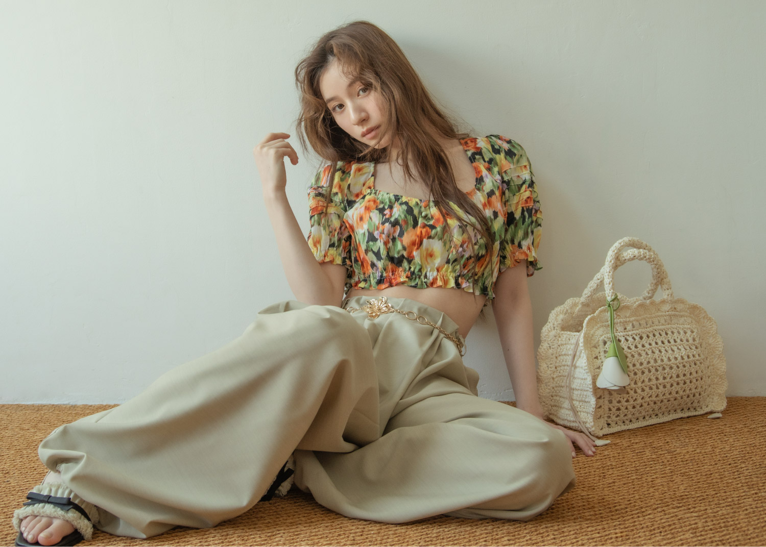 花柄のトップス・ベージュのパンツ・ゴールドのバンツ・ブラックのサンダルを着用した女性