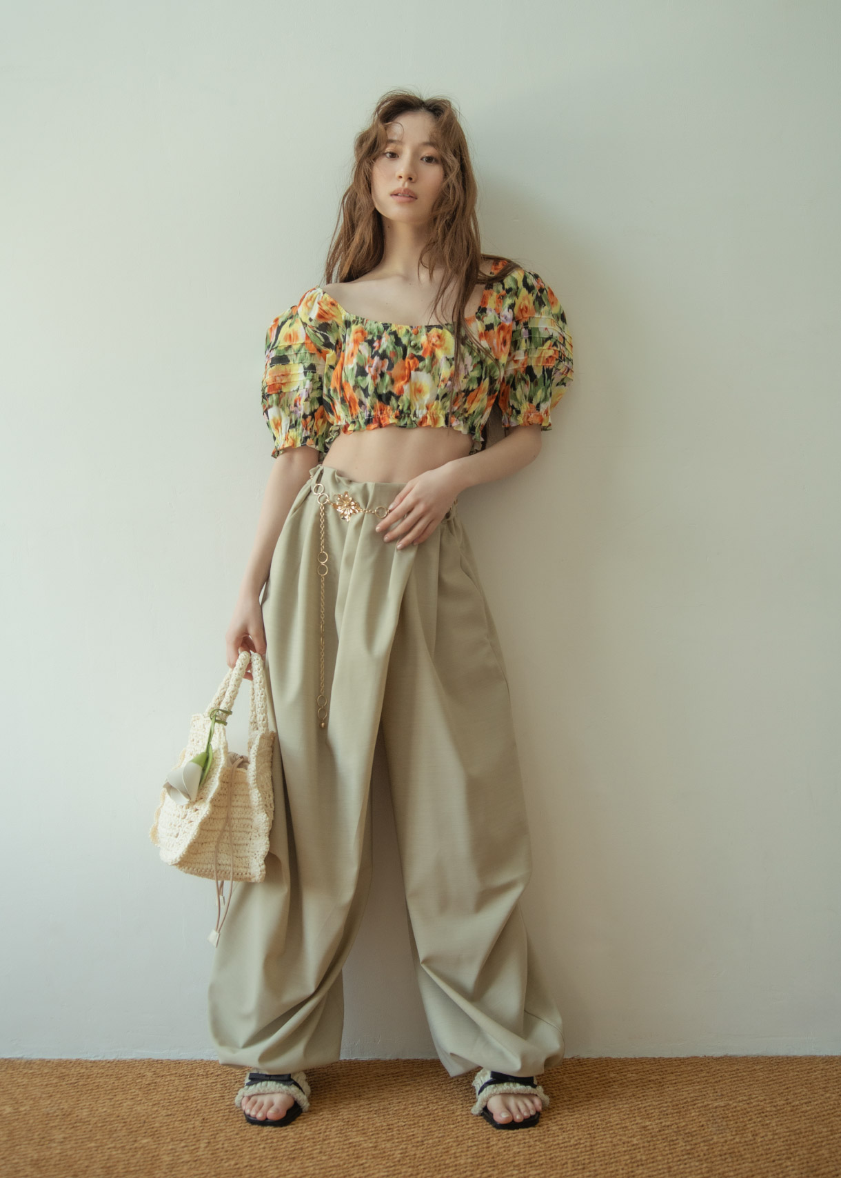 花柄のトップス・ベージュのパンツ・ゴールドのバンツ・ブラックのサンダルを着用した女性