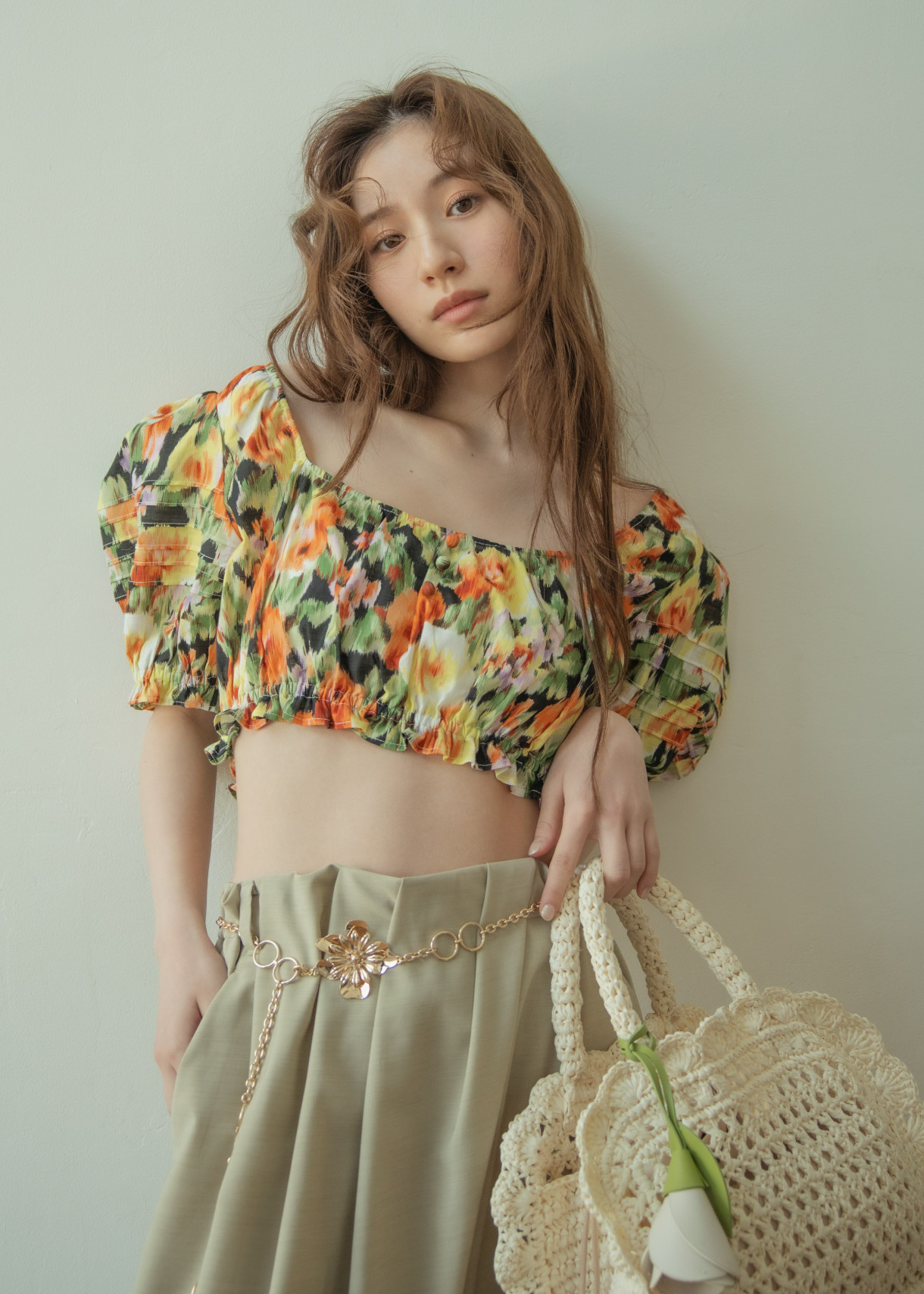 花柄のトップス・ベージュのパンツ・ゴールドのバンツ・ブラックのサンダルを着用した女性