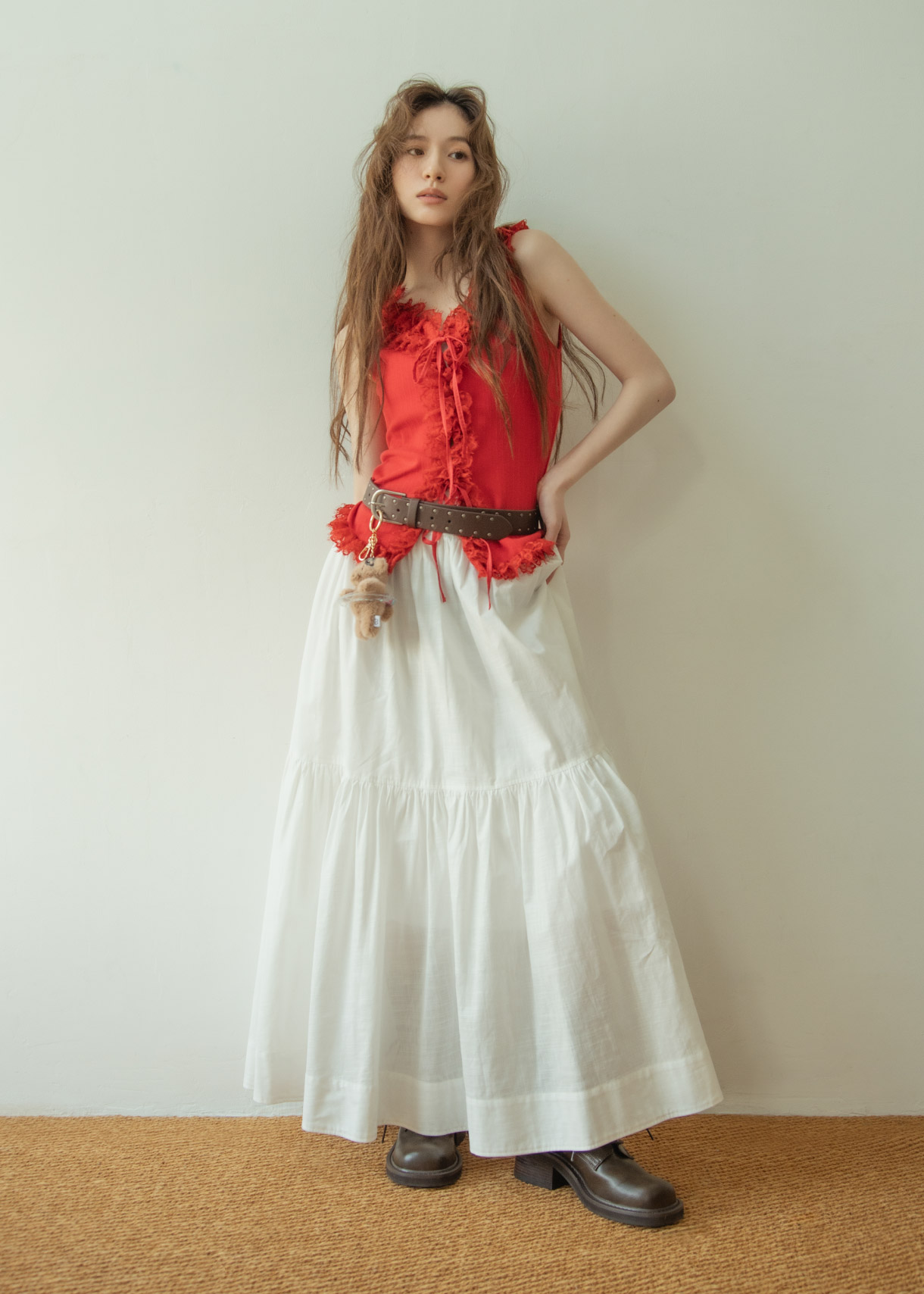 レッドのトップス・ホワイトのスカート・ブラウンのベルト・ブラウンのブーツを着用した女性