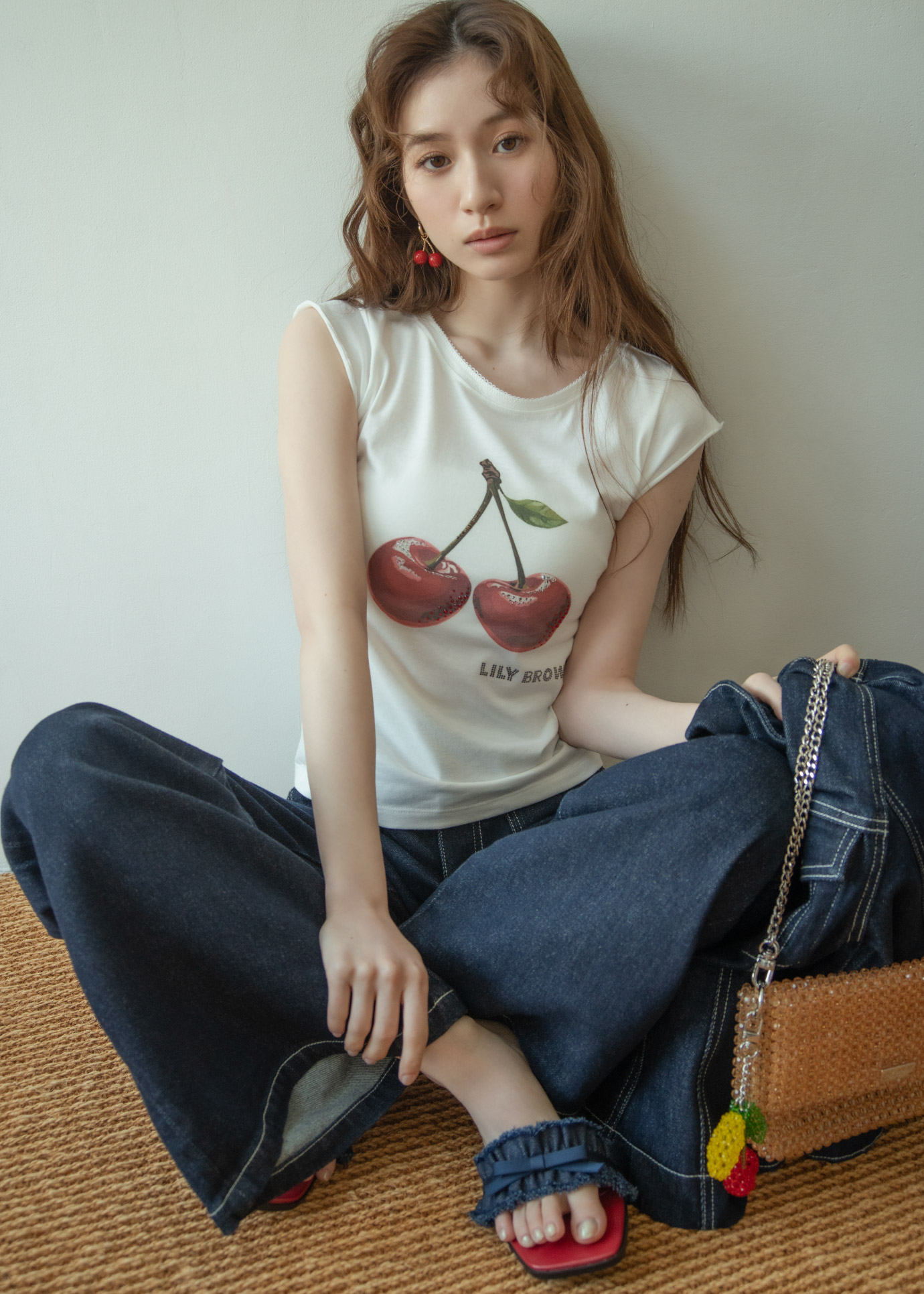 ネイビーのデニムジャケット・チェリーのイラストホワイトのトップス・ネイビーのデニムパンツ・デニムサンダル・ブラウンのバッグを着用した女性