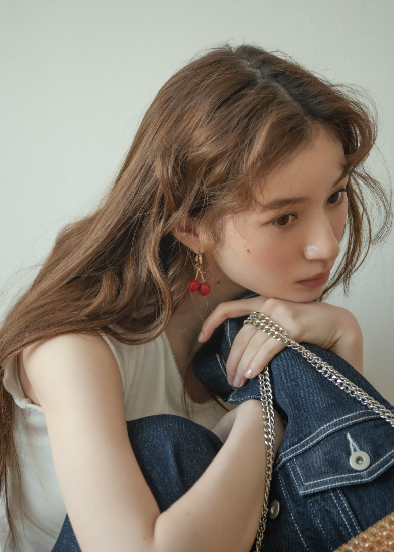 ネイビーのデニムジャケット・チェリーのイラストホワイトのトップス・ネイビーのデニムパンツ・デニムサンダル・ブラウンのバッグを着用した女性