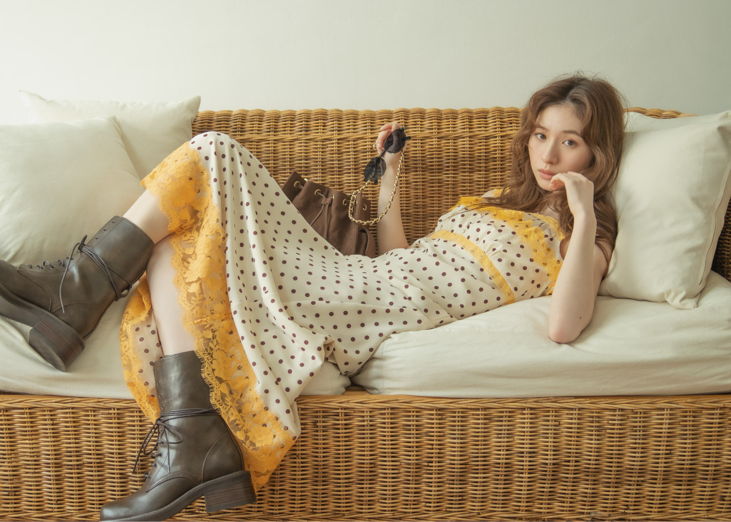 ホワイトとイエローとブラックのドットワンピース・ブラウンのブーツ・ブラウンのバッグを着用した女性