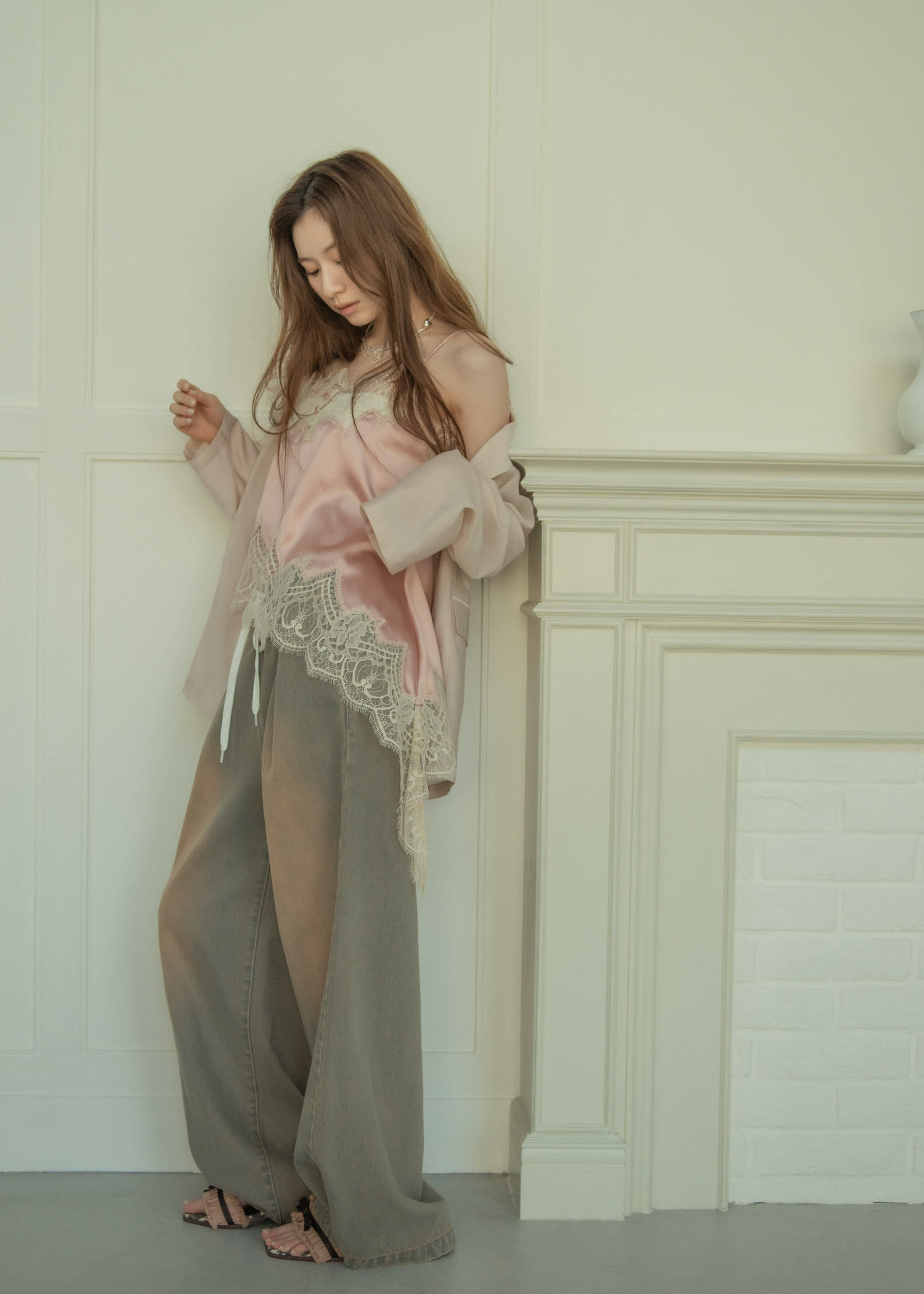 ライトピンクのジャケット・ピンクのトップス・ヴィンテージ感のあるライトブルーのパンツ・シルバーのネックレス・ブラックのサンダルを着用した女性