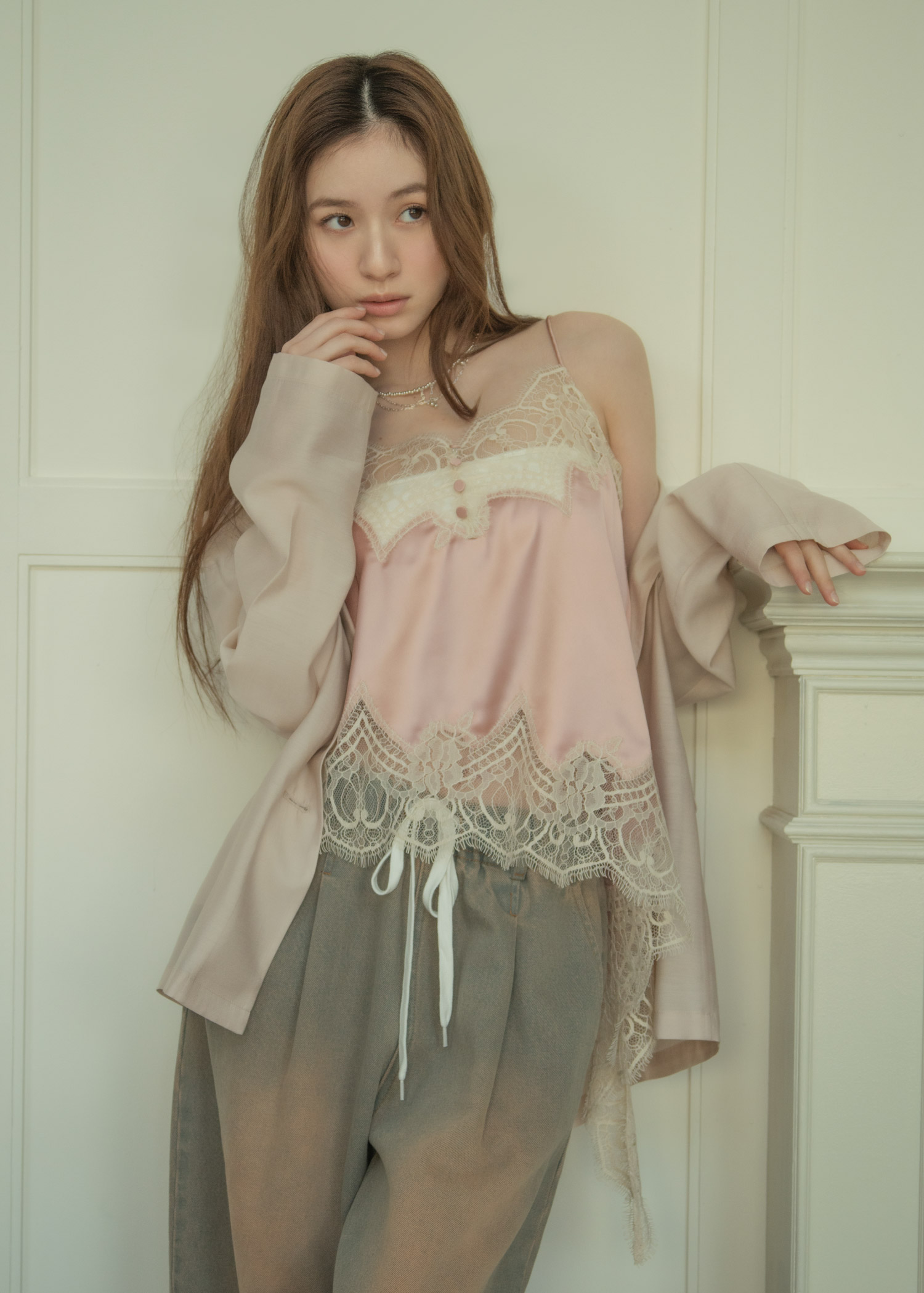 ライトピンクのジャケット・ピンクのトップス・ヴィンテージ感のあるライトブルーのパンツ・シルバーのネックレス・ブラックのサンダルを着用した女性