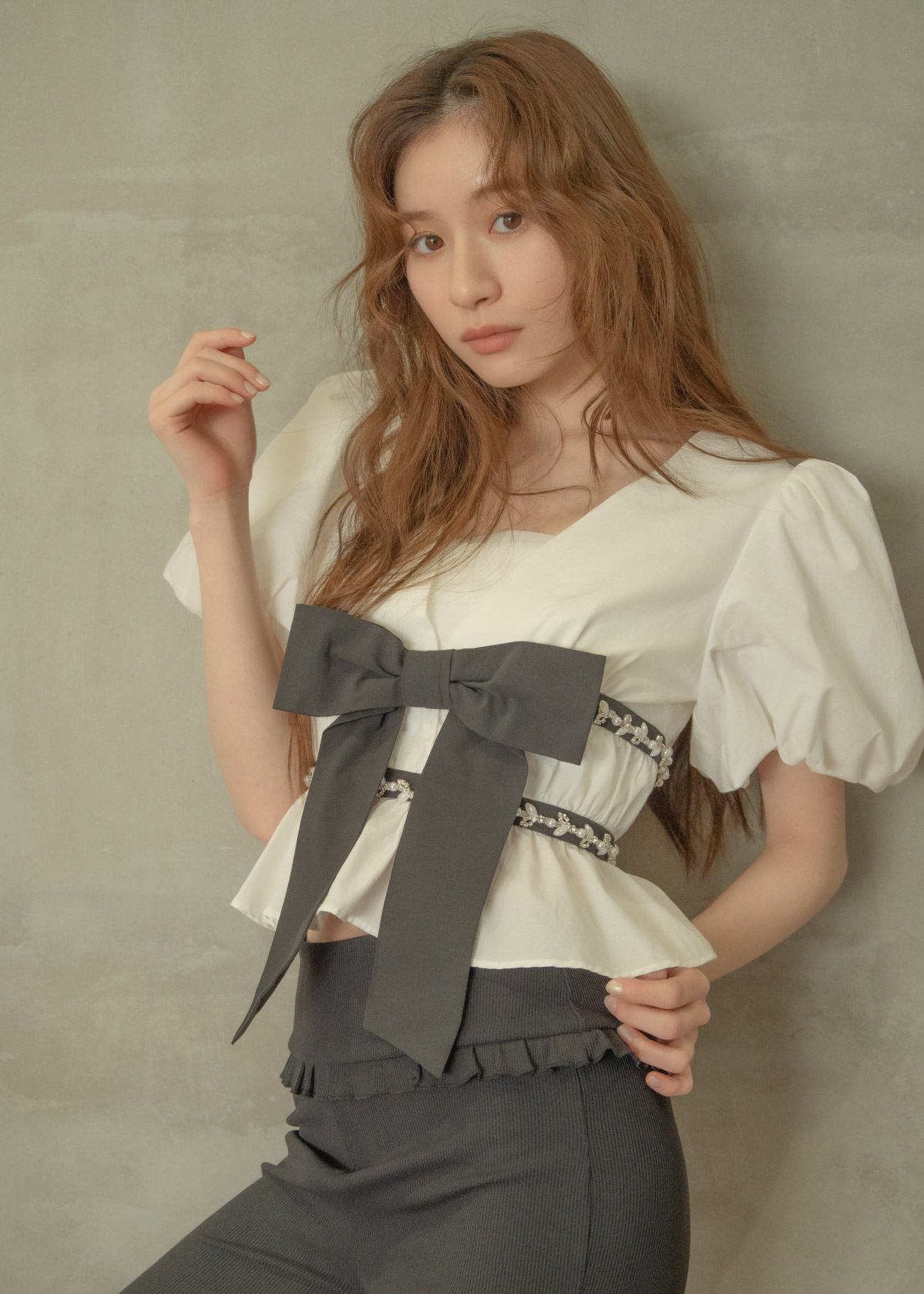 ホワイトのリボン付きのトップス・チャコールグレーのパンツ・ブラックのヒールを着用した女性