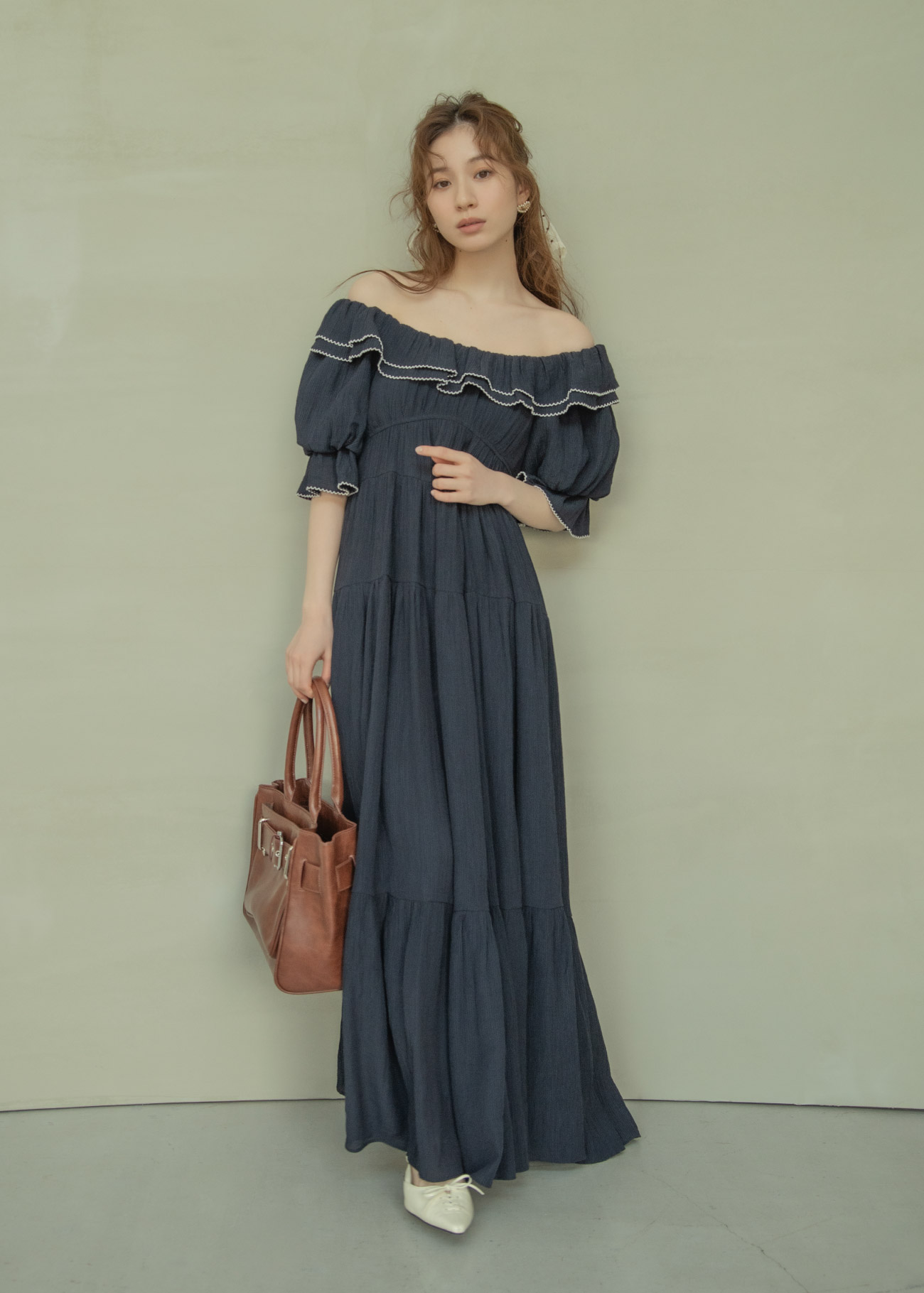 ブラックのドレス・ホワイトのドットのヘアアクセサリ・ブラウンのバッグ・ホワイトのパンプスを着用した女性