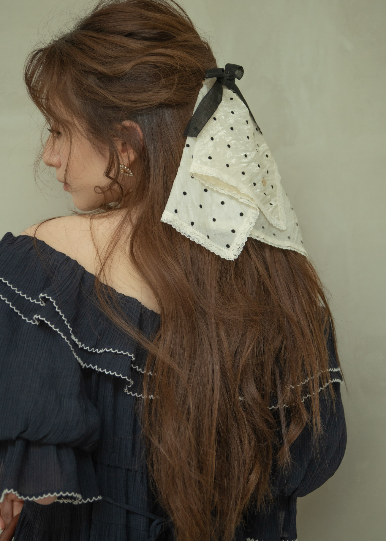 ブラックのドレス・ホワイトのドットのヘアアクセサリ・ブラウンのバッグ・ホワイトのパンプスを着用した女性