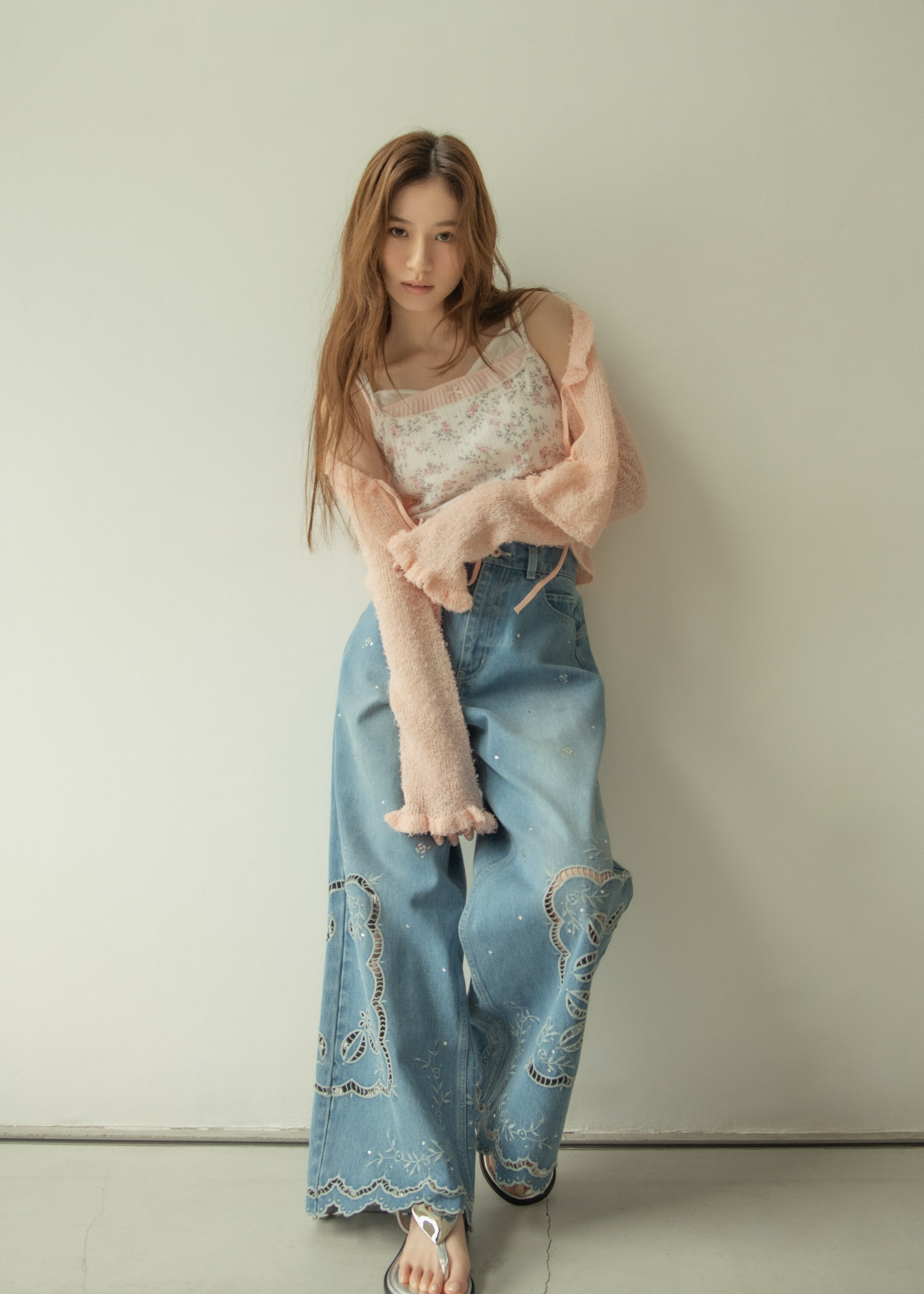 ライトピンクのカーディガン・花柄のトップス・ライトブルーのデニムパンツ・サンダルを着用した女性