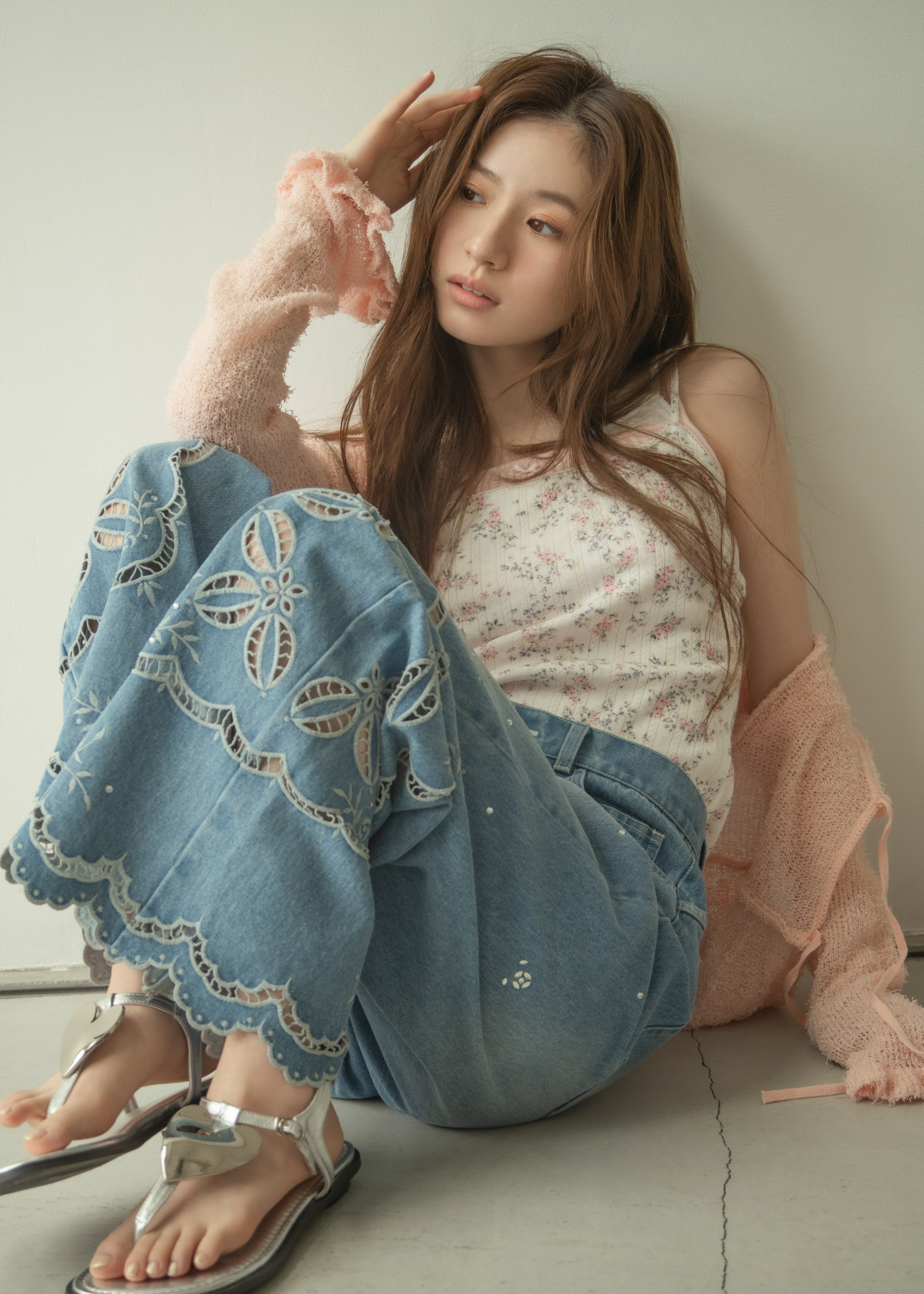 ライトピンクのカーディガン・花柄のトップス・ライトブルーのデニムパンツ・サンダルを着用した女性