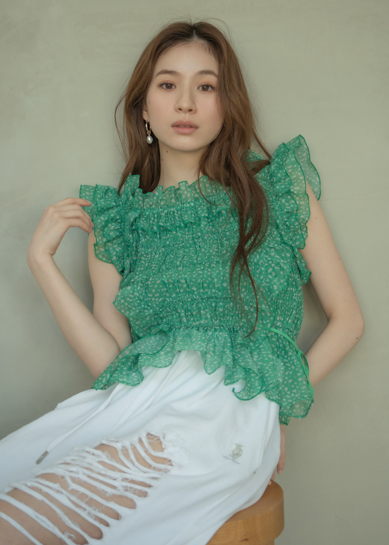 グリーンのブラウス・ホワイトのパンツ・ゴールドのピアスを着用した女性