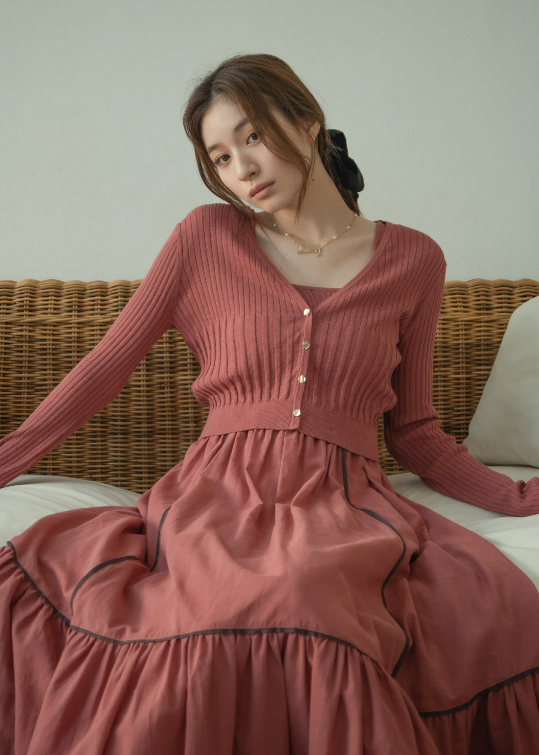 くすんだピンクのカーディガン・ドレス・ヘアアクセサリ・ネックレスを着用した女性