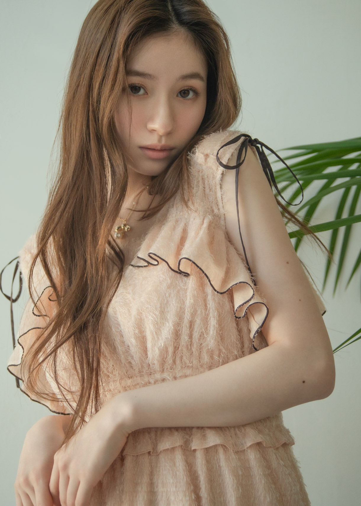 肩のリボンとフリルが特徴的な淡いピンクのロングワンピースに、白のパンプスを合わせた女性のコーディネート。