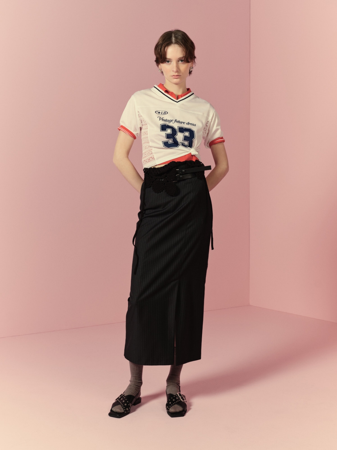 サイドレースナンバリングTシャツ・シアーニットポロシャツ・ダブルベルトタイトスカート・クロシェニットトップス・ヴィンテージハートピアス・バックルフラットサンダルを着用した女性